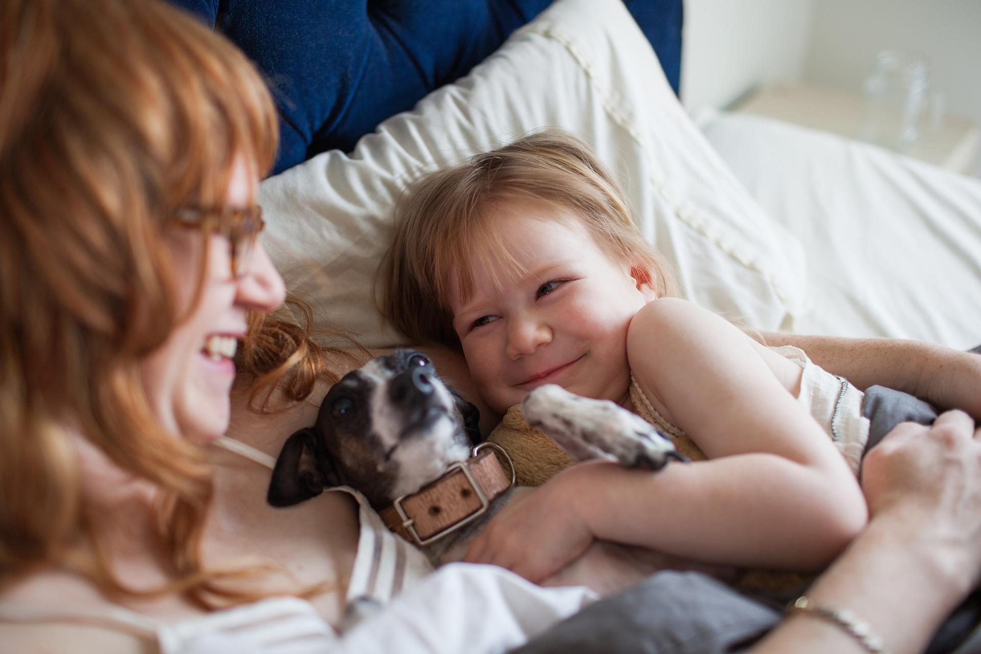 Mother, daughter and dog lying in bed smiling